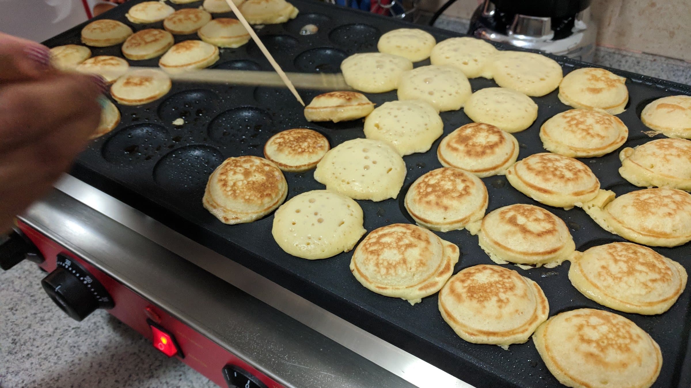 Dozens of golden Dutch mini pancakes cooking on a traditional poffertjes griddle at a Cincinnati event